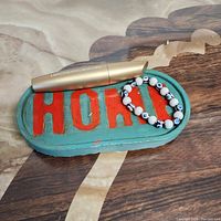 Jewelry holder tray with the word HOME in orange on a teal base, showing belongings placed on it for size reference.