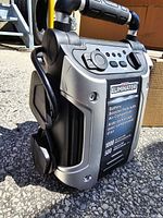 Side angled view showing the battery booster pack's handle, control panel and attached air compressor hose.