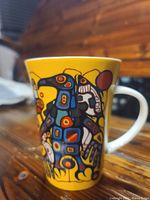 Side view of ceramic mug with detailed Thunderbird art print and visible handle, showing vibrant yellow background.