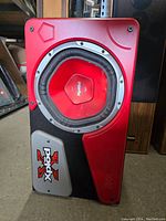 Front view of the Sony Xplod subwoofer showing the red cone, metal ring, and logo plate on the angled red and black enclosure.