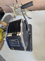 Left side view showing crank handle, multiple number wheels, and label on the side with warnings and instructions.