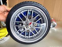 Front view of vintage wall clock designed like a car wheel and tire, showing glowing numbers and hands on clock face.