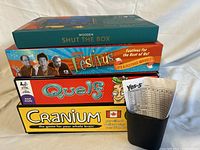 Stacked boxed games Shut the Box, Festivus, Quelf, Cranium with small cup holding papers