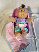 Cabbage Patch doll sitting in pink carrier with blanket