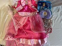 Full view of pink child's Cinderella dress, staff, two Cinderella purses, and child's jewelry including bracelets and bead necklaces.