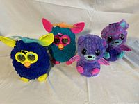 Four electronic toys shown together: two Furby in blue and two purple Hatchimal Twins.