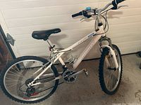Side view of entire white girls' mountain bike with Infinity branding, showing front fork, tires, seat, and handlebars.
