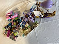 Wide angle photo of LEGO pieces scattered on white surface, showing hot air balloon, dragon, small vehicles, minifigures and loose parts.