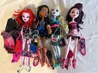 Four Monster High dolls posed together with accessories including two skateboards, handbags, boots, and hairbrush on white background.