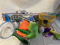 Outdoor play kit items arranged leaning and lying on neutral fabric background, showing kites, nets, ball, and case.