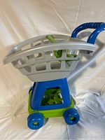 Side view of plastic kids’ grocery cart showing basket, wheels, and handlebar