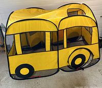 Side and top perspective view of yellow school bus play tent showing mesh windows and printed wheels.