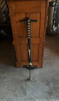 Photo of a black pogo stick leaning against wooden furniture, showing the full height and arm grips, taken to illustrate condition and item identity.