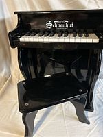 Front view of black wooden Schoenhut child’s play piano with piano seat in front