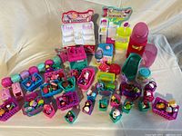 Overview of two Shopkins play structures with numerous small Shopkins figures and accessories organized in colorful baskets and containers arranged on a table.