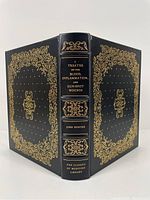 Full view of the front cover, back cover, and spine of the book showing the black leather binding with intricate gold gilt decoration and lettering.