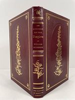 Front and back cover visible showing full burgundy leather binding with gilt decorative floral and leaf designs and gilt stamped title and author on spine.