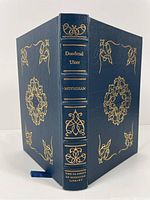 Full view of the book closed showing dark blue full leather binding with gilt decoration and lettering on spine and covers, including silk bookmark.