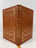 Front and back cover of the book showing full leather binding with gilt embossed decorative floral and scroll motifs, gilt lettering on spine and silk bookmark.