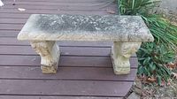Front view of the antique stone bench showing detailed carved supports and weathered stone top.
