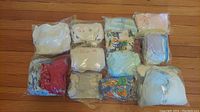Multiple Ziploc-sealed bundles of baby clothes arranged in rows on a wooden floor, showing variety in colors and sizes.