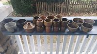 Wide view of all ceramic items including various bowls and cups arranged on shelf outdoors