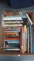 Box packed with assorted children's books, mostly hardcover and some softcover, showing spines with various titles.