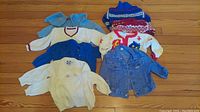 All items of the children's clothing lot laid out on a wooden floor showing the various sweaters and jackets.