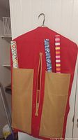 Hanging gift wrap organizer front view showing two large tan pockets holding three rolls of gift wrap paper in assorted patterns (multi-colored circles, blue and white swirls, pink and red stripes)