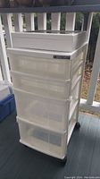 Front and left side view of the white plastic 4 drawer rolling cart with wooden box on top taken outdoors showing all drawers and caster wheels.