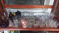 Front view showing entire assortment of various small glass jars, bottles, and cups on wooden shelf.