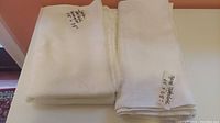 Two folded white linen tablecloths placed side by side, one appears plain and the other with visible damask pattern.