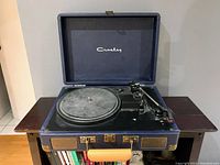 Front angle photo of open Crosley briefcase record player showing platter, tonearm, control knobs, and built-in speakers.