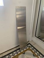 Door kick plate leaning against wall, showing length and brushed metal finish.