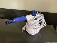 Photo of a blue and white handheld steam cleaner resting on a dark surface with its power cord wrapped around its body.
