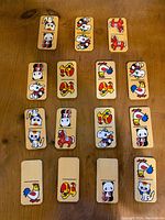 Top-down photo of 16 wooden rectangular game pieces laid out showing colorful cartoon animal and character images on each.