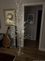 Whole lit tree showing the white LED lights on the branches and birch bark texture of trunk.
