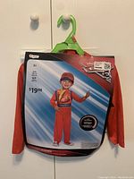 Photo of a toddler Lightning McQueen costume in original packaging, labeled size 2T, featuring a smiling toddler model in an orange jumpsuit with race decals.