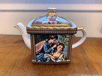 Front view of the Limoges tea pot featuring a painted scene of two women and floral lid decoration with gold accents.