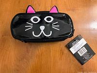 Front view of a new black pencil case with a printed cat face and pink ears, showing retail tag.