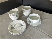Nine pieces of white porcelain dishes with black floral pattern arranged on a table including bowls, plates, cup and saucer.