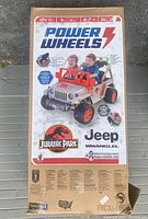 Retail box front showing product image, Jurassic Park and Jeep Wrangler logos, Power Wheels branding and key features.