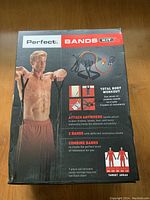 Box front showing a shirtless man demonstrating arm workout with resistance bands, highlighting total body workout use, band attachments, 2 bands with different resistance levels, combined use for resistance level, and target areas.