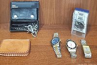 View of all watches and accessories together on wooden surface showing four wristwatches, black chain wallet, and tan leather pouch.
