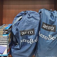 Two blue AeroBed inflatable mattresses in storage bags and Pure Comfort queen size air bed box on shelf.