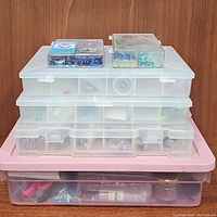 Stacked clear plastic storage boxes with various compartments containing beads and crystals in assorted colors