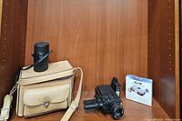 Lot consisting of black Sankyo camera, brown carrying case, Sony recorder, camera accessories, and film box on wooden shelf