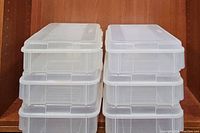 Stack of six clear plastic storage containers with hinged lids shown stacked in two columns of three.