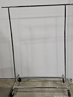 Front view of the adjustable single bar metal garment rack with caster wheels on concrete floor.