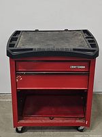 Front view of red Craftsman tool chest showing 2 closed drawers, open bottom compartment, black plastic worktop, and caster wheels.